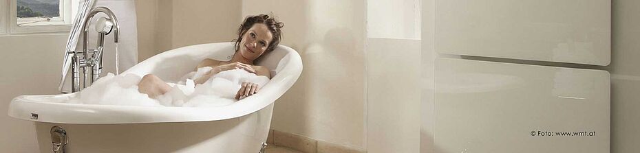 Frau liegt gemütlich in der Badewanne, an der Wand ist die Infrarotheizung zu sehen